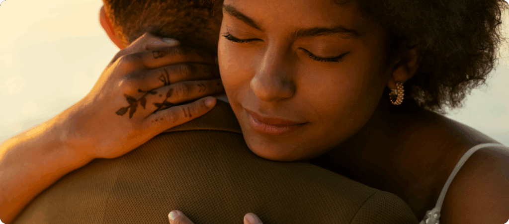 A woman hugging a man with the sun setting behind them.