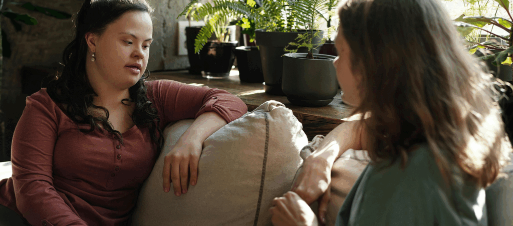 Two women sitting on a couch having a conversation, one woman with Down syndrome, appearing to be in a counseling session.