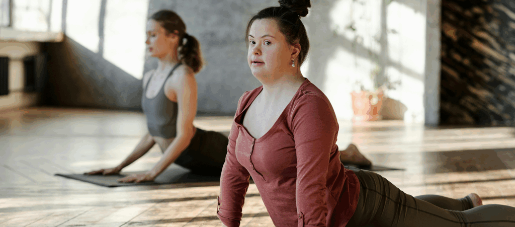 A girl with Down syndrome doing stretching exercises with another girl behind her.