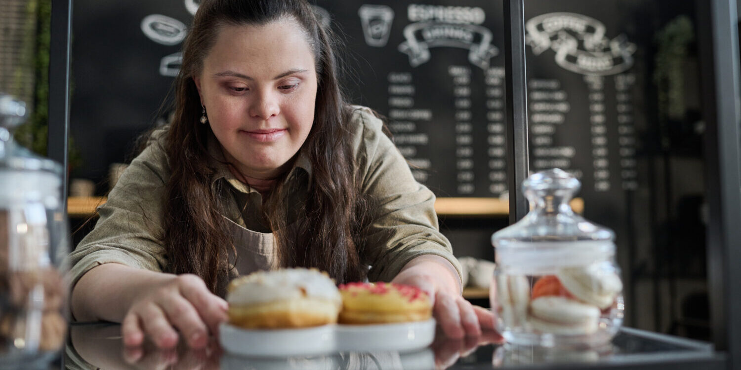 Waitress putting tasty donuts on tray A young girl with Down syndrome working at a café.